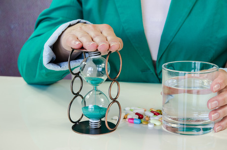human hands and colorful pills , sandclock and glass of water
