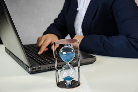 female hand typing in notebook and sandglassの写真素材