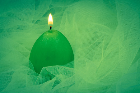 green burning candle over green fabric backgroundの写真素材