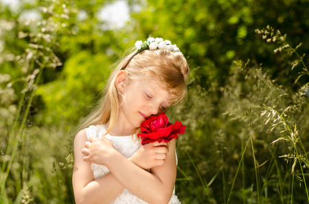 beautiful blond little girl with flower headband holding red roseの写真素材