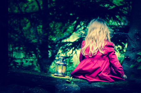 girl with long blond hair with lantern sitting in dark woodsの写真素材
