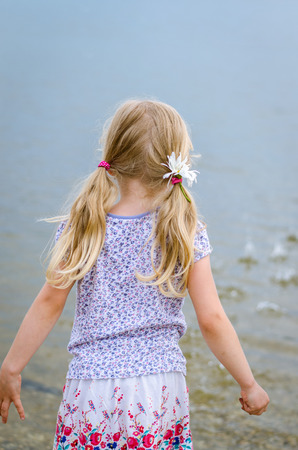 girl with long hair throwing stones into water back viewの写真素材