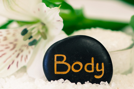 white sea salt, white flower and black lava stone with words body
