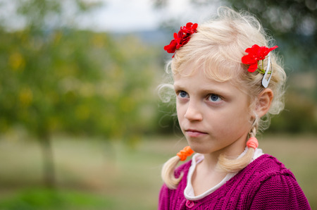 adorable caucasian blond girl with braids and red chrysanthemum flower on hairの写真素材