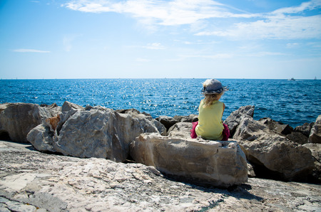 little girl sitting in the rock observing blue seaの写真素材