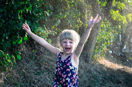 smiling little blond girl in spray water during hot summer dayの写真素材