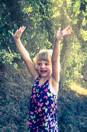 smiling little blond girl in spray water during hot summer dayの写真素材