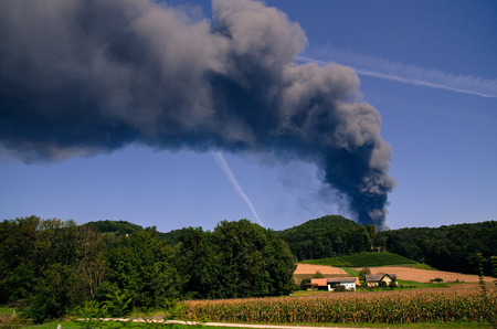 smoke from fire in blue sky above green landscape