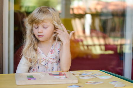 little blond girl with bandage on shoulder playing with puzzleの写真素材