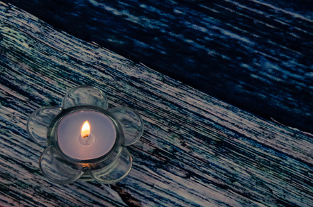 burning candle in candleholder with shape of flower against blue wooden backgroundの写真素材