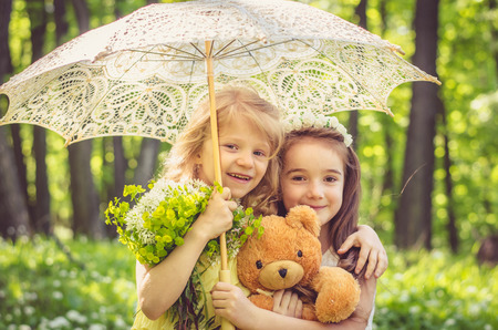two beautiful girl friends holding teddy bear toy under umberlla in the spring forest の写真素材