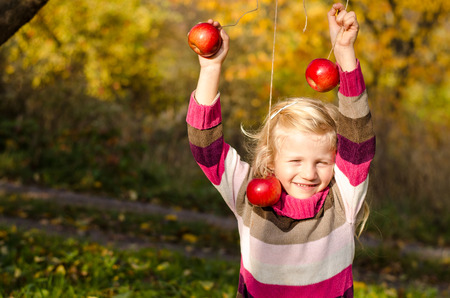 beautiful blond long haired girl with red apple in autumn timeの写真素材