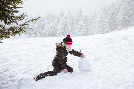 little girl in the forest building the snowmanの写真素材