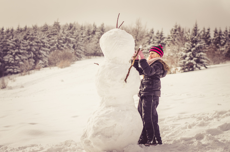 little girl in the forest building huge snowmanの写真素材
