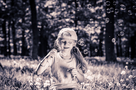 cute blond girl in the forest having fun blowing soap bubbles monochromeの写真素材