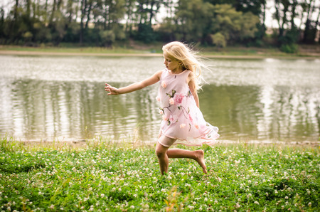 beautiful caucasian girl with long blond hair in pink dress dancing as the fairy in the green grass by the riverの写真素材