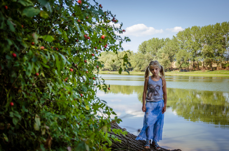little girl walking under tree branches by the river bankの写真素材