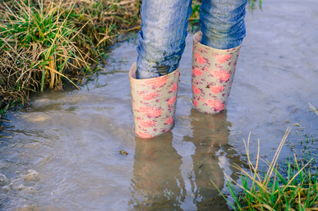 legs of child in pink rubber boots standing in water puddle
