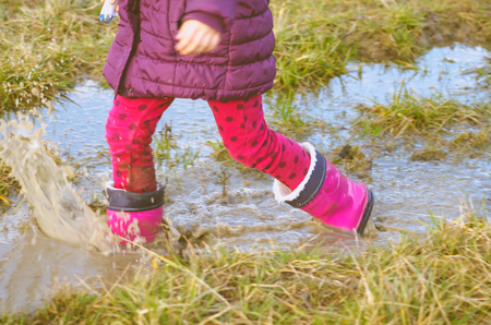 little girls legs walking and jumping in water pool in meadow