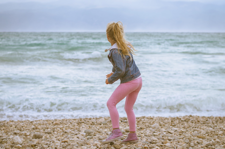 little lovely blond girl throwing stones into the seaの写真素材
