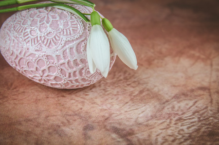 white snowdrop flower and pink easter egg decoration on brown fabric backgroundの写真素材