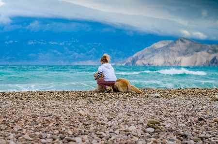 little blond girl with dog in rocky beach in the Croatian coast looking to the sea horizonの写真素材