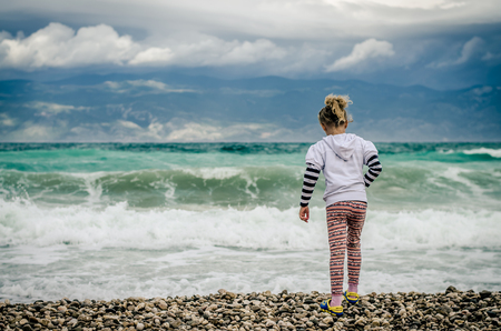 little lovely blond girl throwing stones into the heavy seaの写真素材