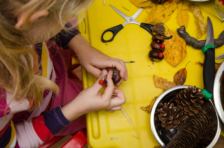 little child making autumn decoration from chestnut, pine cones and acornsの写真素材