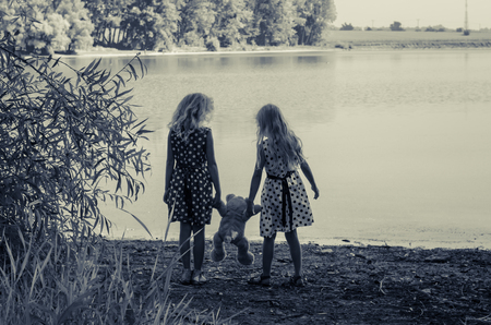 two little girls with long blond hair holding a teddy bear toy の写真素材
