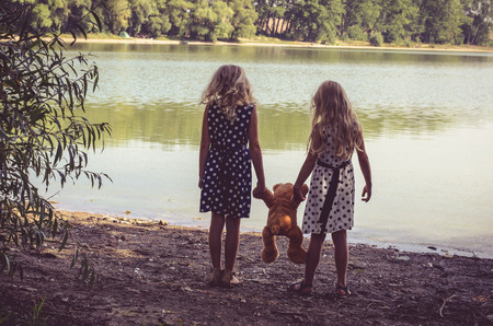 two little girls with long blond hair holding a teddy bear toy の写真素材