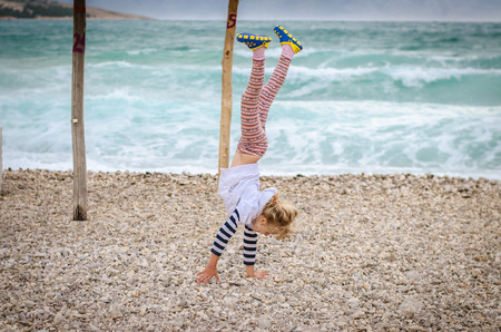 little blond girl doing gymnastics in the rocky beach by the seaの写真素材