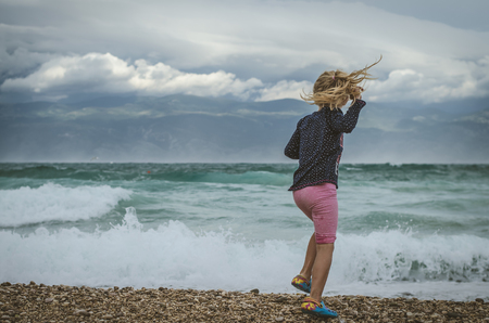 happy little girl playing with sea on the rocky Croatian beach in windy weather の写真素材