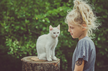 adorable blond girl and white cat together outdoors in the gardenの写真素材