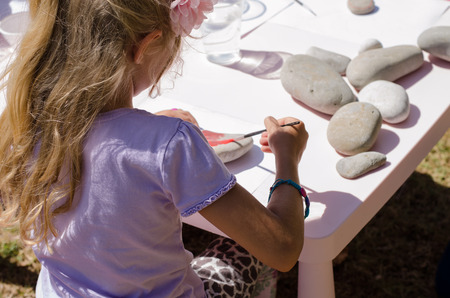 cute little blond girl with long hair having fun painting stonesの写真素材