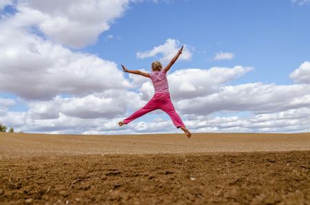 little child jumping alone in country in scenic countryside with beautiful clouds and blue skyの写真素材