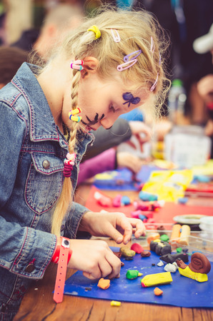adorable blond girl playing with play dough and creating figure on the tableの写真素材