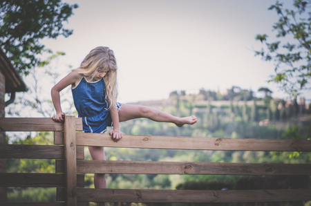 adorable little child sitting at the wooden fence in green nature in beautiful romantic italian Tuscanyの写真素材