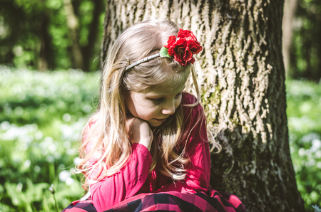 lovely blond girl sitting by the tree trunk in the forestの写真素材