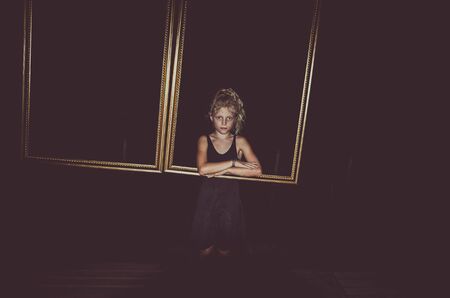 little child behind empty frame in dark black background at nightの写真素材