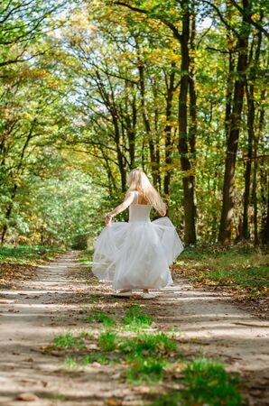 cute little girl in long white wedding dress walking in magic forestの写真素材