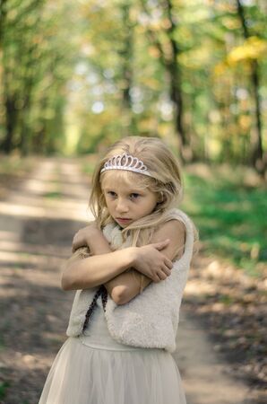 one little girl in dress freezing in path among autumnal trees in forest in golden hour atmosphereの写真素材