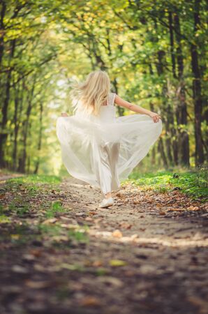 one little girl in dress posing in path among autumnal trees in forest in golden hour atmosphereの写真素材