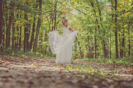 one little girl in dress dancing in path among autumnal trees in forest in golden hour atmosphere