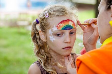 Little lovely girl waiting for rainbow face painting to be done