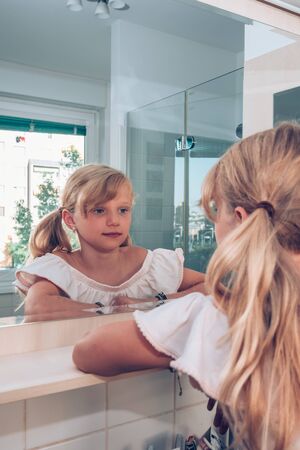 close up portrait of tidy beautiful girl with braid hairdo looking into bathroom mirror