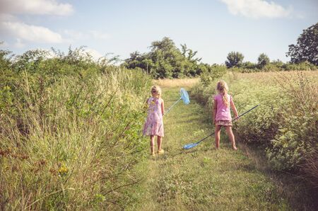 two little children with nets in hand catching butterflies in green countrysideの写真素材