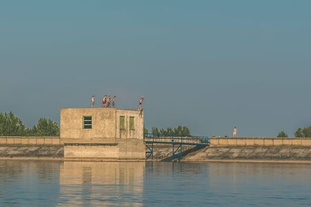 brave boys jumping from the roof of the building in the rocky barrier into the blue water of rural pondeの写真素材
