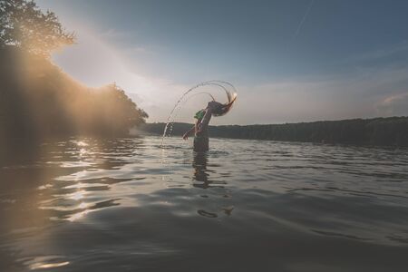 cute girl with long blond hair posing as model in water in golden hour timeの写真素材