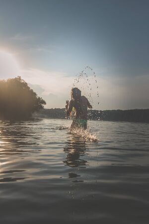 cute girl with long blond hair having fun in pond in magic golden hour timeの写真素材