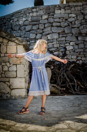 adorable child with long blond hair in blue dress having romantic time in historic streets back viewの写真素材